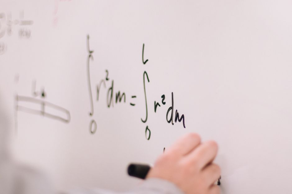Person writing math equations on a whiteboard, focusing on integrals and formulas.